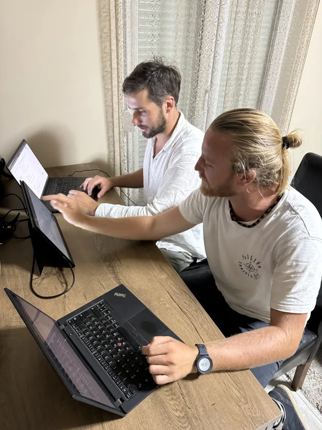 Two people working together on laptops at a dining table.